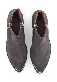 Stivaletti alla caviglia in suede grigio con punte rialzate, zip argento ai lati e interno in pelle marrone. Presentano una suola nera slim.