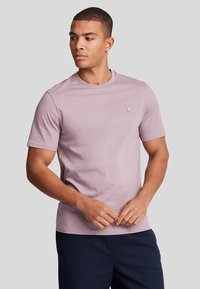 Maglietta in cotone di colore lilla chiaro con collo a giro e maniche corte, caratterizzata da un piccolo logo ricamato sul petto.