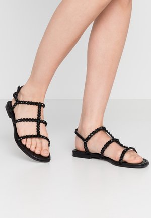Sorte flade sandaler med en stroppedesign og runde perler. Stropperne har en tekstureret overflade, med en simpel, minimalistisk sål.