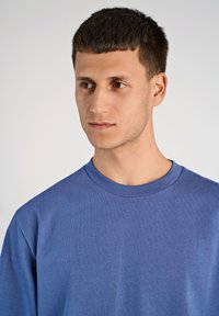 Maglietta a girocollo blu realizzata in tessuto misto cotone, con maniche corte e superficie liscia, indossata da una persona con capelli corti.