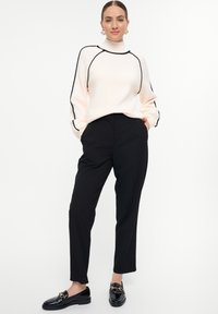 Suéter crema con ribete negro, cuello alto y mangas largas, combinado con pantalones negros ajustados y mocasines negros brillantes.