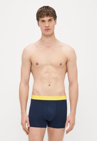 Boxers azul-marinho feitos de algodão, com cintura elástica amarela onde está impresso "HAPPY". Textura suave e corte ajustado.