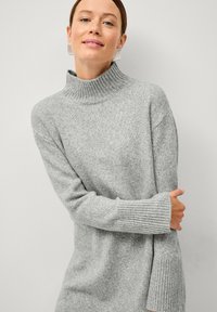 Pull col roulé gris clair en maille douce, avec des poignets larges côtelés et une coupe décontractée légèrement surdimensionnée.