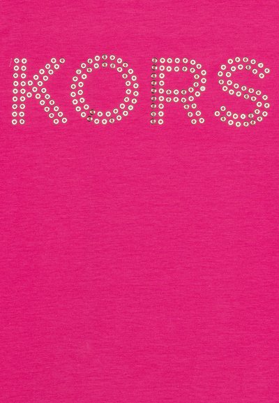 Camiseta rosa con la palabra "KORS" en grandes tachuelas metálicas circulares. La tela tiene una textura sutil, creando un impacto visual vibrante.