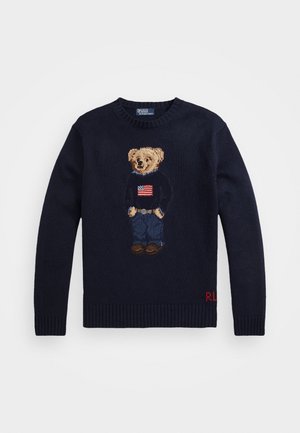 Laivastonsininen neulepaita, jossa seisova nallekarhu, jolla on päällään neulepaita, jossa on Amerikan lippu, farkut ja ruskeat kengät. RL-alkukirjaimet alareunassa.