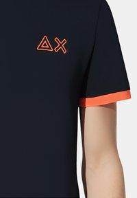 T-shirt blu navy con dettagli arancioni sulle maniche; presenta un logo geometrico ricamato in arancione sul petto.