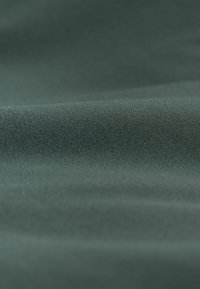 Dunkelgrüner Stoff mit einer glatten, strukturierten Oberfläche. Die Webart ist dicht und zeigt unter Licht einen dezenten Glanz. Keine sichtbaren Muster oder Akzente.