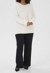 Suéter ligero de crema con cuello redondo y textura acanalada, combinado con pantalones de pierna ancha negros y zapatos negros con punta.