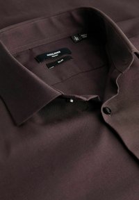 Donkerbruine slim-fit shirt met een soepele textuur, button-down kraag en zwarte knopen. Labels met "JACK & JONES" en maatdetails zichtbaar.