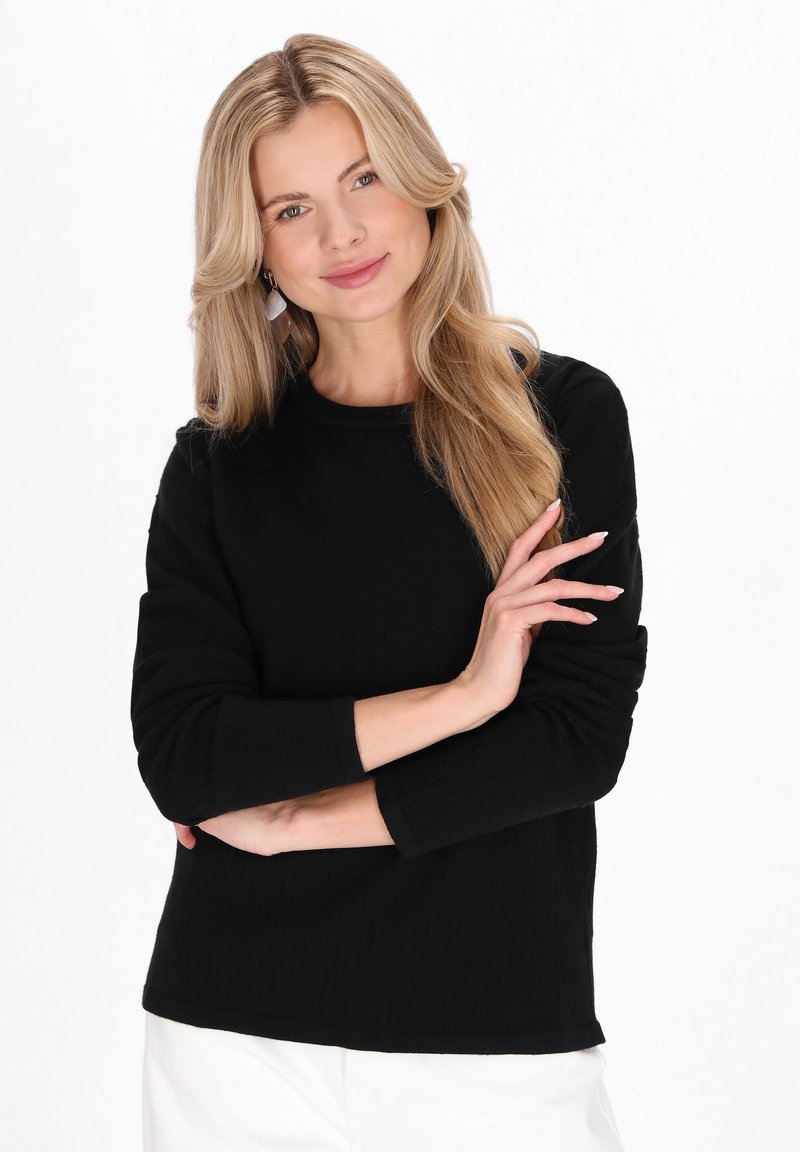 Pulover negru cu mâneci lungi și dungi, cu decolteu rotund. Prezintă o croială lejeră și o textură moale, asortat cu pantaloni de culoare deschisă.