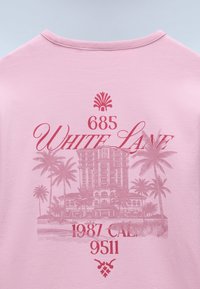 Tessuto rosa con testo rosso "685 White Lane 1987 CAL 9511" e illustrazione di un edificio con palme sullo sfondo.