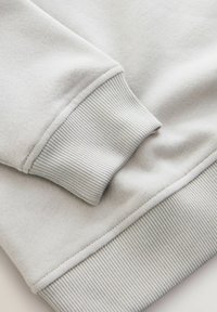 Jasnoszary mankiet bluzy z ribbowanym wzorem; miękka tkanina, staranne szwy i minimalistyczny design podkreślają prostą elegancję.