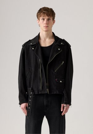 Svart denim motorsykkeljakke med skulderklaffer, glidelåslommer og spenneakenter. Har en avslappet passform og en slitt tekstur. Stylert med svart topp og jeans.