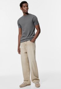 Siva majica kratkih rokavov v kombinaciji z lahkimi bež širokimi hlačami in lahkimi supergami, z ohlapnim krojem in mehko teksturo tkanine.