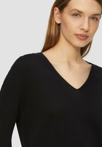 Zwarte V-hals trui met lange mouwen, gemaakt van gebreide stof. Heeft een gladde textuur en een nauwsluitend design. Eenvoudig en minimalistisch.