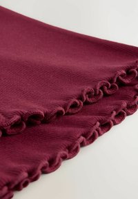 Tissu bourgogne avec une surface texturée, mettant en valeur une bordure froncée le long d'un bord, présentant des motifs ondulés et une apparence douce.