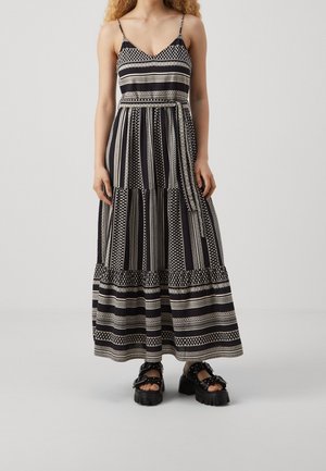 Maxi sukienka w czerni i bieli z mieszanką wzorów w paski. Ramiączka spaghetti i falbaniasty dół dodają lekkości i ruchu. Noszona z sandałami na platformie.