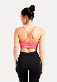 Sujeción deportiva rosa con tirantes cruzados en la espalda y la palabra "SMILODOX" impresa. Combinada con mallas negras de cintura alta.