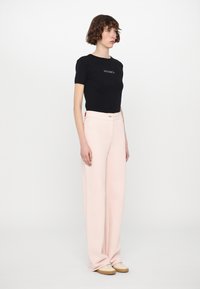 Svart bomulls T-skjorte med "MAX&Co." logo, kombinert med vide lyse rosa bukser og beige sko. Minimalistisk design med subtile toner.