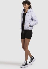 Light purple puffer jacket with a hood, featuring a quilted design and zipper front. Worn over a black crop top and black shorts.