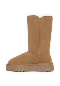 Botas de ante marrón hasta la rodilla con punta redonda, suave forro de piel blanca en la parte superior y suela gruesa de goma. Detalles de costura en el lateral.