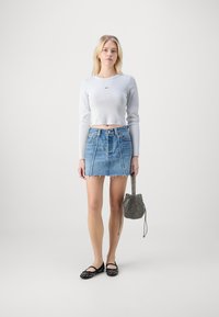 Szürke, hosszú ujjú cropped top, kék farmer mini szoknya, frayed hem rendezéssel, fekete stúdióval díszített balettcipők, és egy kötött, húzószárral ellátott táska.
