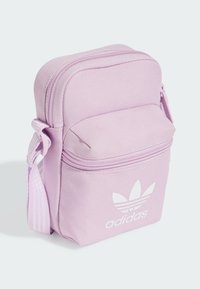 Bolso cruzado de tela rosa con un bolsillo delantero con cremallera. Presenta el logo de Adidas en blanco y una correa ajustable. Superficie texturizada con costuras reforzadas.