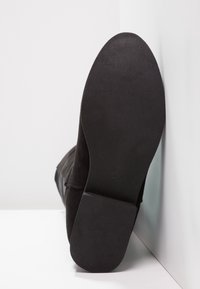 Bota de ante negra con puntera redonda, suela texturizada y tacón plano, mostrando la etiqueta de talla '37' en la suela de goma.