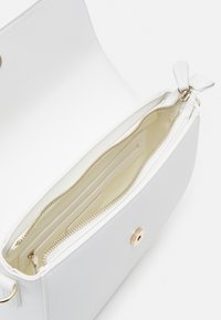 Bílá kožená kabelka s hladkým povrchem, vybavená zipem a uzávěrem v zlatém odstínu. Vnitřní přihrádky pro organizaci.