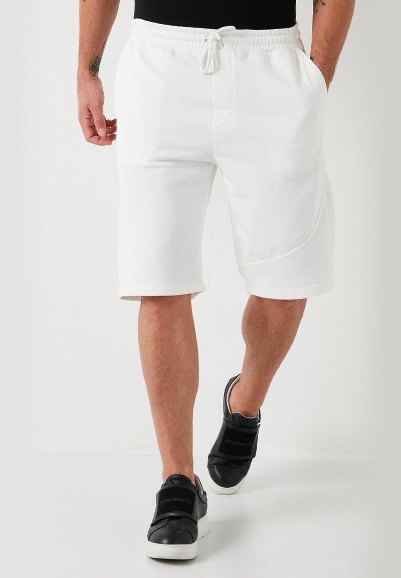 Shorts blancs en mélange de coton avec une taille élastique et un cordon de serrage. Coupe droite, longueur genou, dotés de poches latérales et de coutures minimales.