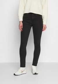 Calças de ganga pretas skinny com uma textura suave. Apresenta uma cintura média e dois bolsos frontais. Acompanhadas de um sweatshirt casual em creme e ténis.