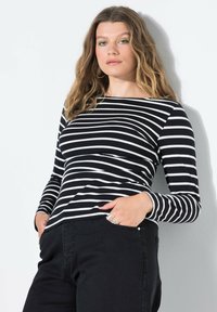 Gestreiftes, schwarz-weißes Langarm-Oberteil mit weitem Halsausschnitt, enganliegender Silhouette, weichem Stoff und subtiler Rippstruktur. Sichtbare schwarze Jeans.