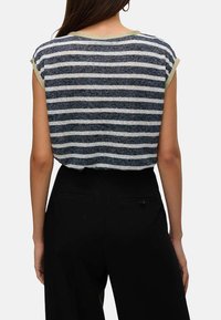 Top en tricot rayé bleu marine et crème, encolure ronde, manches courtes avec un passepoil contrasté, porté avec un pantalon taille haute noir.