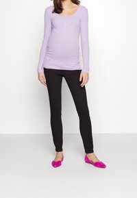 Top de manga larga en color morado claro con botones, combinado con pantalones ajustados negros y bailarinas fucsias, sobre un fondo blanco.