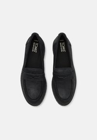 Melni zamšaini loafers ar gludu apdari, ar mīkstu zoli un dekoratīvu izšuvumu malās. Zīmola logotips redzams iekšpusē.