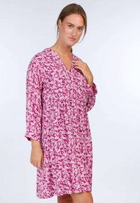 Pink floral dress featuring a V-neckline, three-quarter sleeves, and a relaxed fit with a gathered waistband. Patterned with small white flowers.