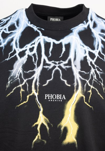 T-shirt nera con una grafica a forma di fulmine in bianco e giallo, con "PHOBIA ARCHIVE" stampato sotto il design. Materiale in cotone.