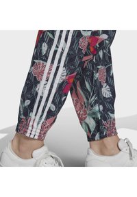 Blommönstrade joggers med mörk bakgrund, som har vita sidostreck och vristmanschetter, matchade med vita sportskor.