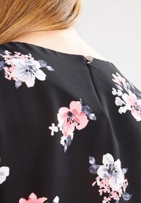 Svart blommig blus med rosa och ljuslila blommor, slät tyg, rund halsringning och en liten silverknapp på baksidan.