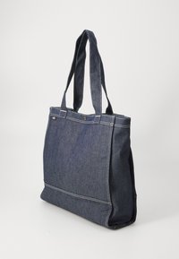 Denim toteväska med två långa handtag, mörkblå färg, kontrasterande vitt stygn, rektangulär form och magnetknäppning.