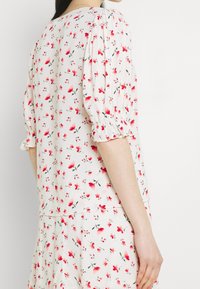 Abito floreale bianco realizzato in un tessuto morbido, con maniche corte a sbuffo, motivi floreali rossi e rosa, e una vestibilità ampia con gonna a strati.