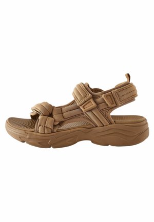 Tan sport sandal med teksturerede stropper, justerbare spænder og en polstret sål med et bølget mønster for bedre greb.