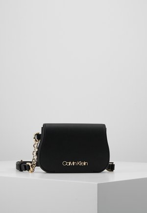 Schwarze Calvin Klein Umhängetasche mit gewölbter Klappe, goldenem Logo auf der Vorderseite und verstellbarem Schulterriemen aus goldener Kette und Leder.