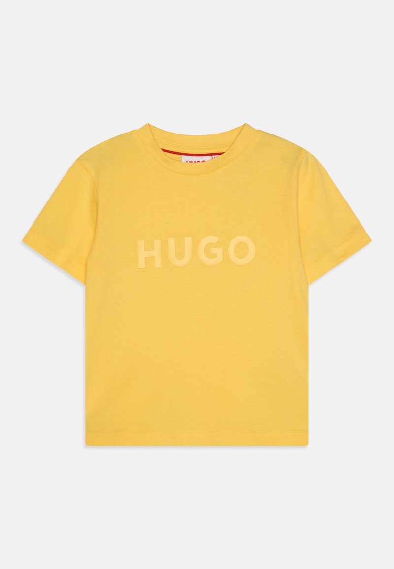 Geltonas medvilnės marškinėlis su apvalia kaklo iškirpte ir trumpomis rankovėmis. Priekį puošia žodis "HUGO" šiek tiek tekstūruotu, kontrastiniu šriftu.
