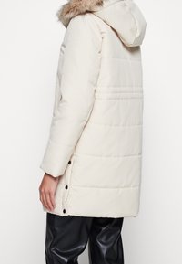 Giubbotto bianco in stile piumino con cappuccio e bordo in pelliccia sintetica removibile. Presenta un design trapuntato, chiusura con bottoni a pressione e tasche laterali.