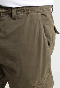 Khaki cargo shorts, joissa on teksturoitu kangas, säädettävä vyötärö, sivutaskut ja vahvistetut saumat kestävyttä varten.