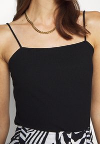 Zwart geribd hemdje met dunne bandjes, met een vierkante halslijn. Gecombineerd met een patroonrok met strepen in zwart en wit. Gouden ketting.