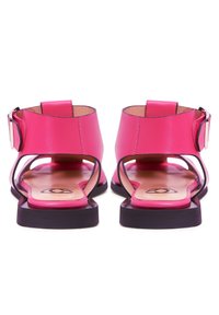 Růžové kožené sandály s kotníkovým popruhem, otevřenými stranami a plochou černou podrážkou. Vyznačují se hladkým povrchem a decentním logem na stélce.
