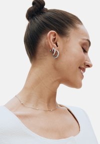 Zilveren oorringen met afwisselend gladde en met strass bezette accenten. Een delicate zilveren ketting met kleine kralen. Gestructureerde witte top.