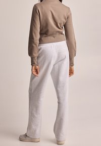 Felpa cropped marrone chiaro e pantaloni tuta grigi, realizzati in tessuto morbido, con una tasca sul retro. I pantaloni hanno una vestibilità rilassata e una vita elastica.